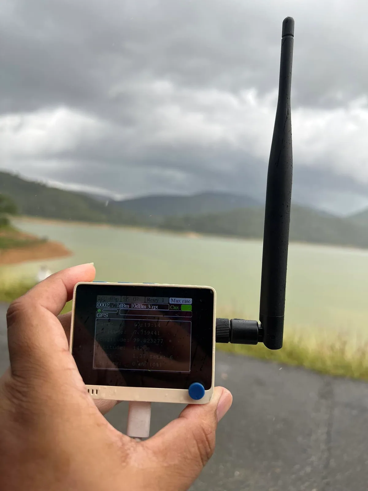 A handheld LoRaWAN tester and antenna in front of a reservoir and mountains during Southern IoT’s field survey.